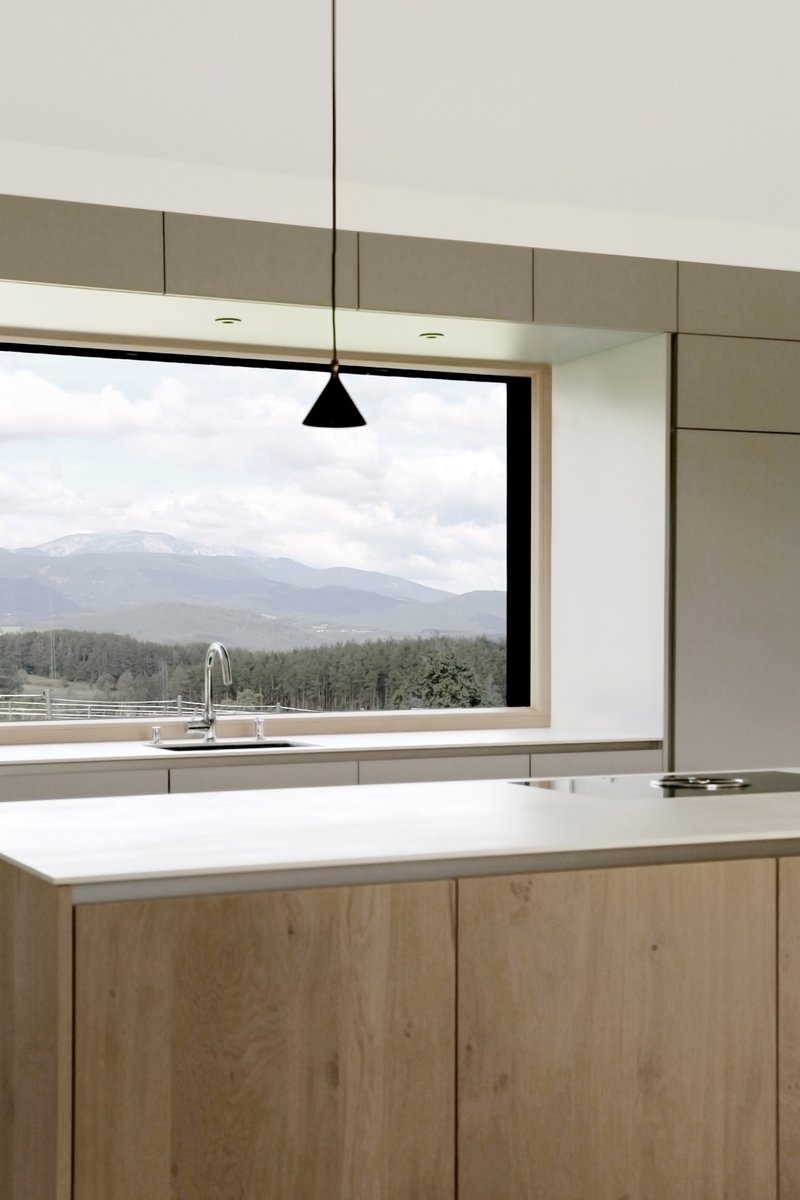 Kitchen island with light timber cabinetry and horizontal window framing a view of forested mountains