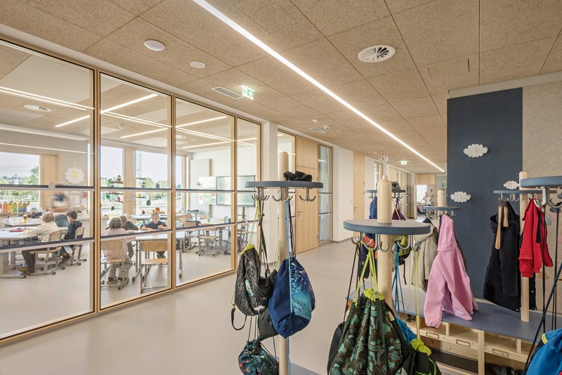 Interior hallway with coat hooks and glazed partition looking into adjacent classroom spaces