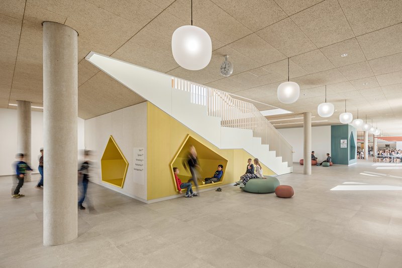 Open hall with white staircase and yellow triangular reading nooks beneath it with children seated