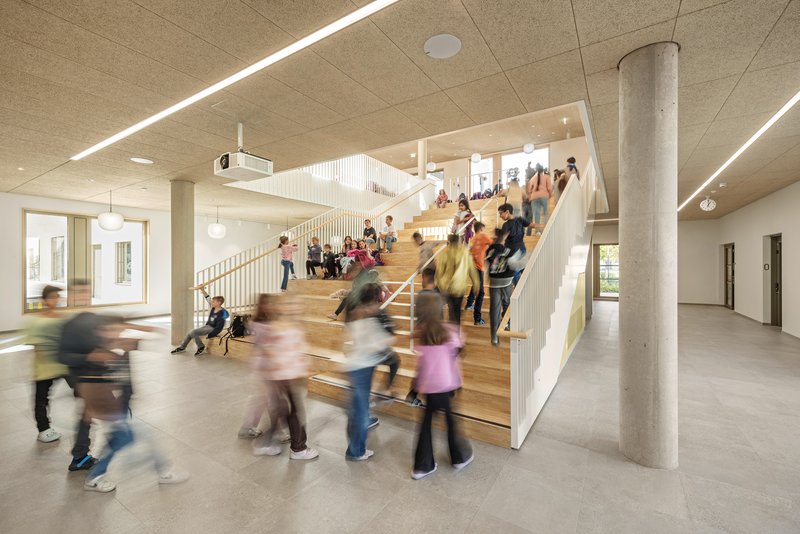 Wide timber staircase with children seated and moving through the double-height circulation space