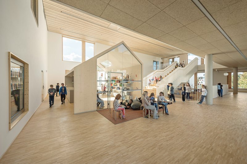 Open floor plan with house-shaped plywood volumes and children gathered on timber flooring