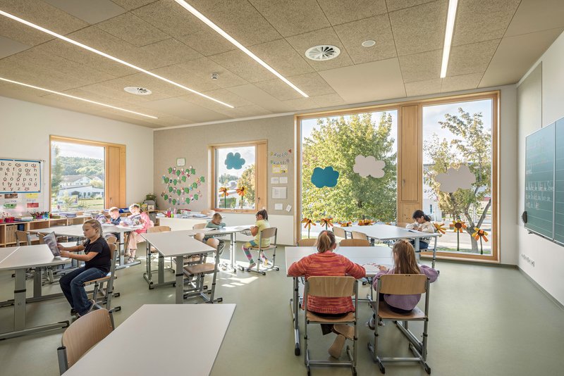 Classroom with white desks and large timber-framed windows overlooking trees in autumn foliage
