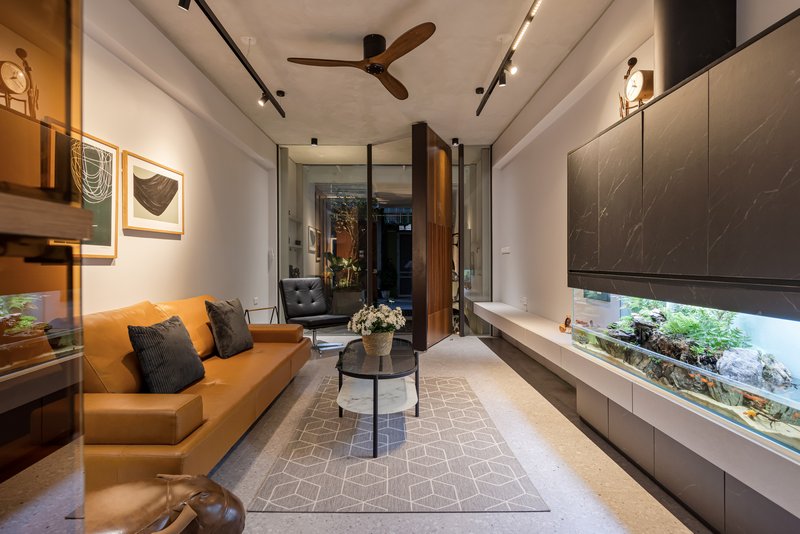 Long view of living room with tan leather sofa, dark marble media wall, and terrazzo flooring under track lighting