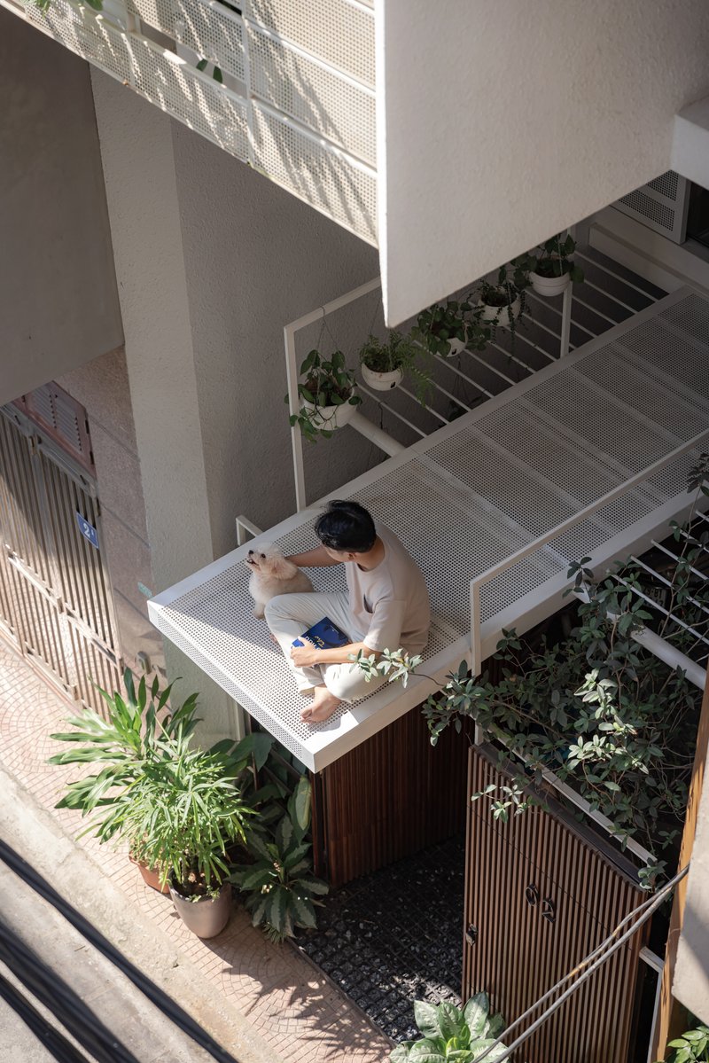 Overhead view of resident seated on perforated metal balcony platform surrounded by planters and pebble ground