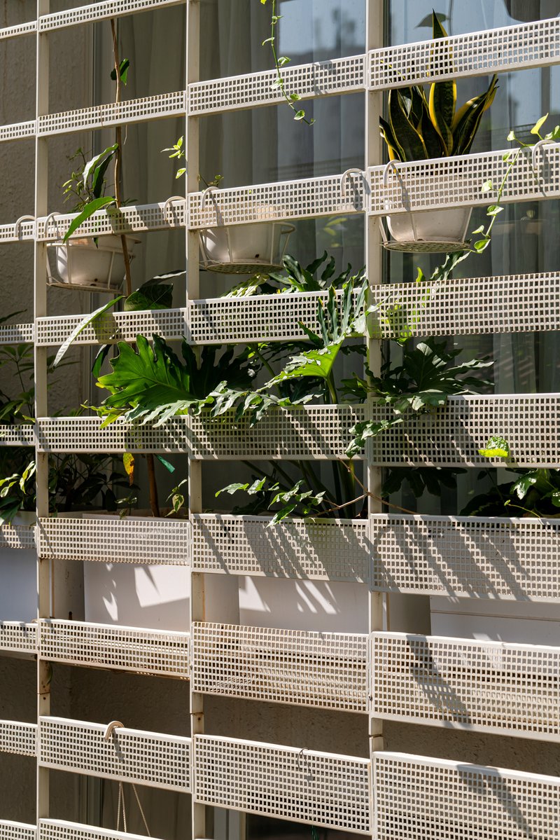 Facade detail of stacked white perforated metal screens with tropical plants growing between the horizontal bands