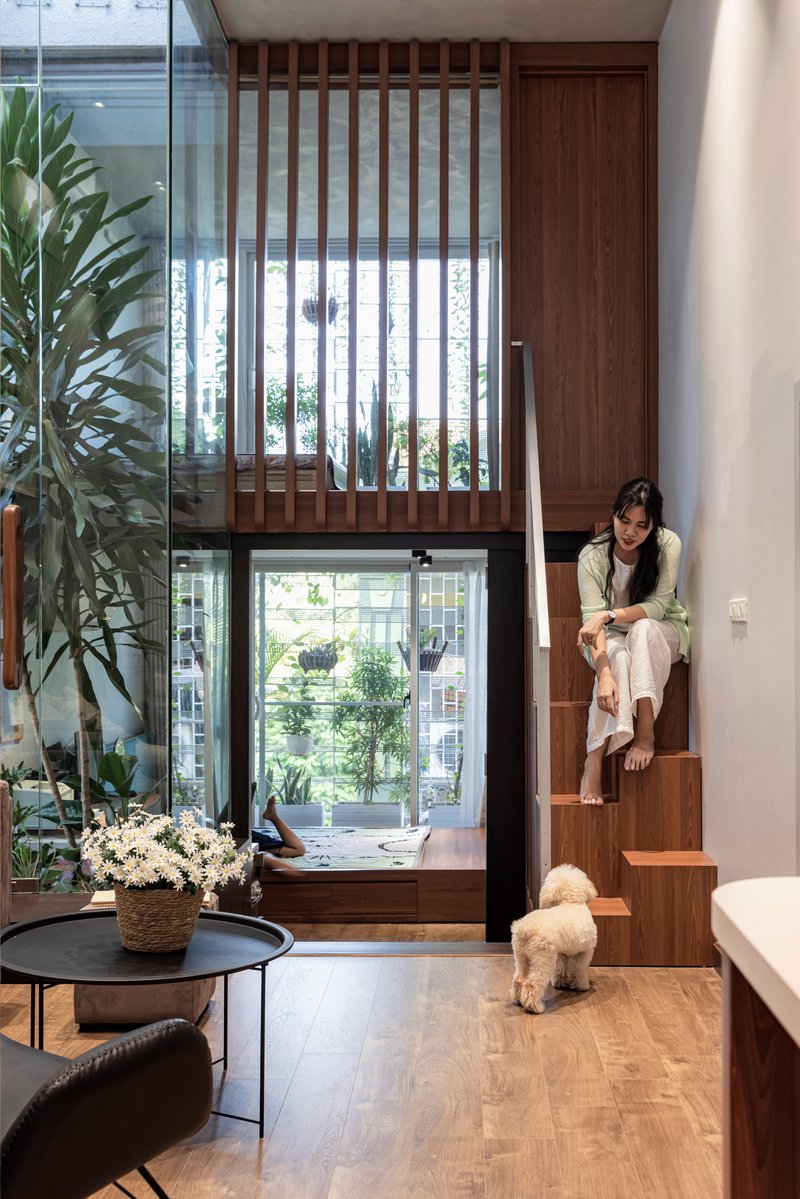 Double-height living room with timber slatted screen and woman seated on wooden stair beside dog