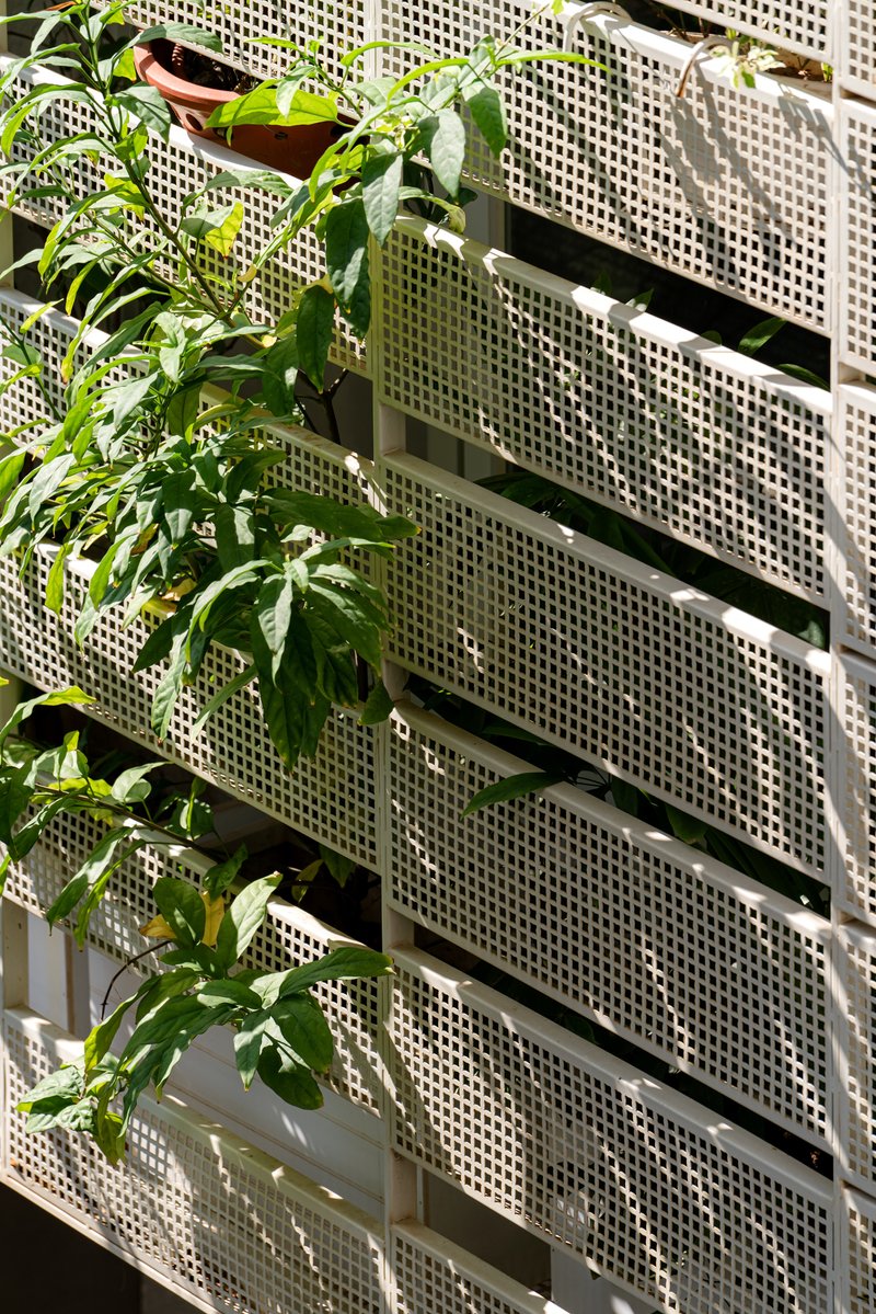 Perforated white metal screen panels with planted balconies visible through the openings