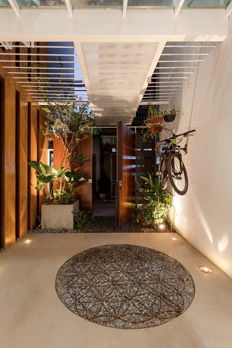 Entry courtyard at dusk with circular pebble feature, timber screens, and potted plants under perforated ceiling