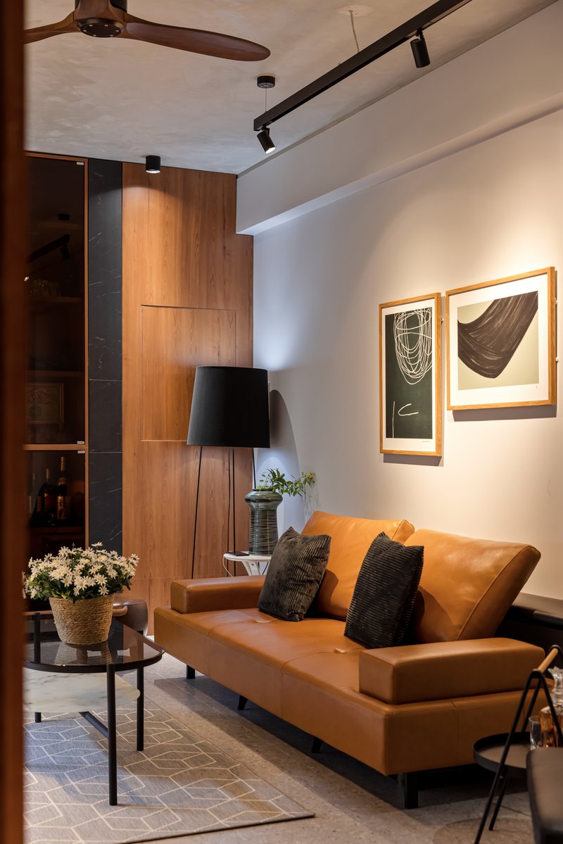 Corner of living room showing tan leather sofa, timber storage wall, and framed artwork under track lighting