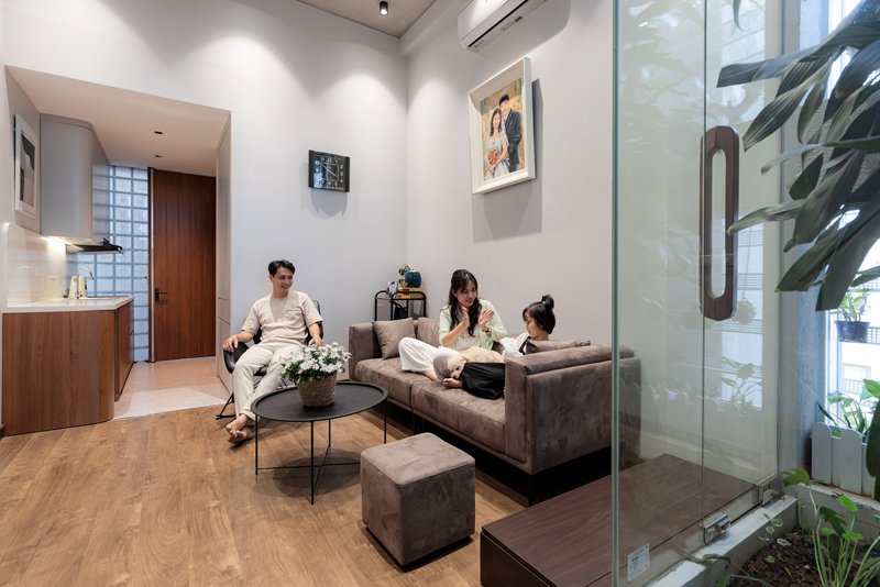 Seating area with grey sofa and three residents beside a glass-walled courtyard with planted greenery