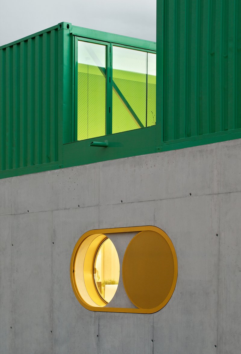 Close-up of yellow circular portal in concrete paired with green shipping container window above