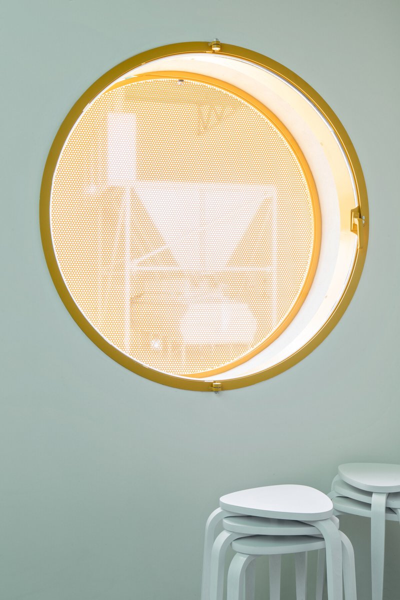 Circular window with yellow metal frame and perforated screen on pale green interior wall