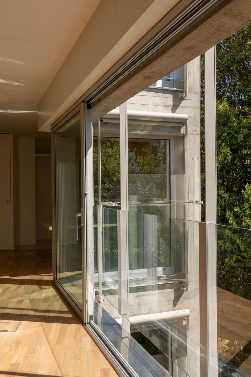 Interior view through sliding glass doors opening to a glazed exterior elevator shaft and planted wall