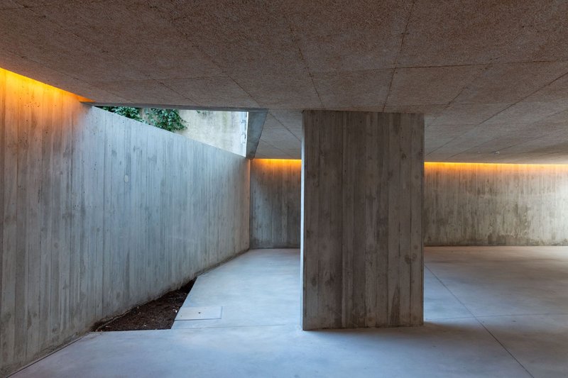 Board-formed concrete carport with indirect lighting strips illuminating walls and ceiling at dusk