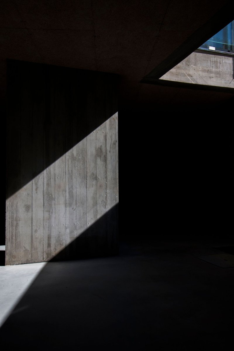 Diagonal light cutting across a darkened interior space with board-formed concrete walls