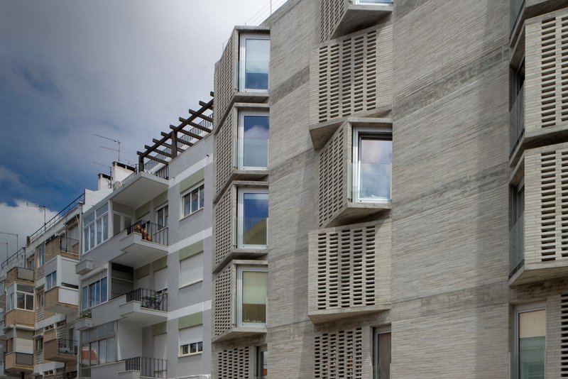 Street view of the layered concrete facade with projecting bay windows and horizontal louvered panels under an overcast sky