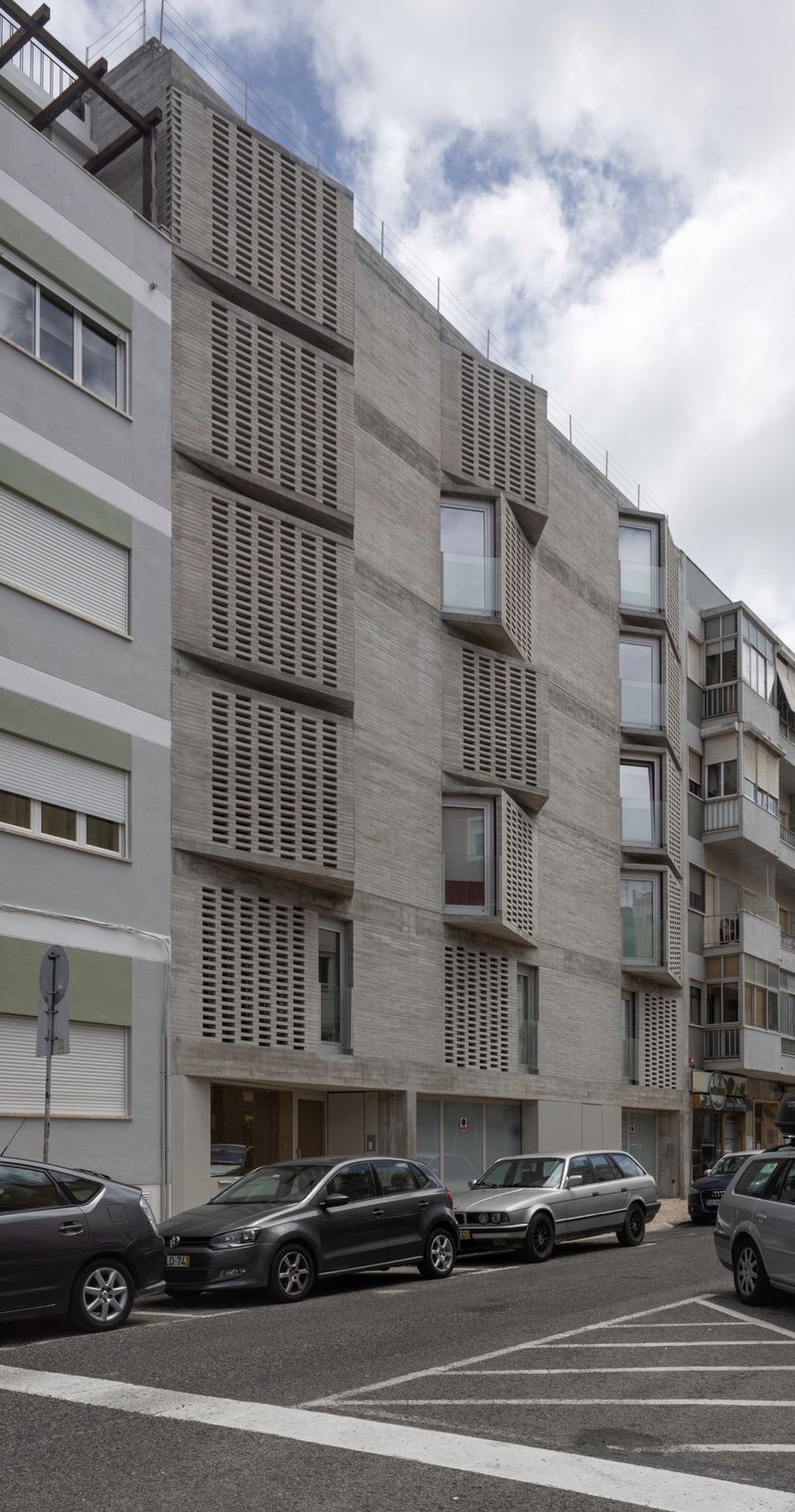 Full elevation showing alternating concrete and perforated screen panels beside parked cars on the street below