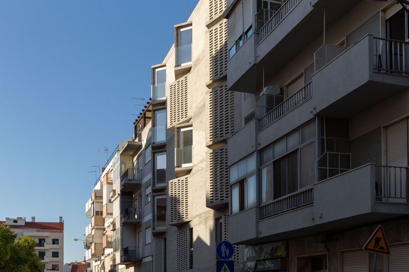 Street facade with cream-colored perforated brick towers and balconies under a clear blue sky