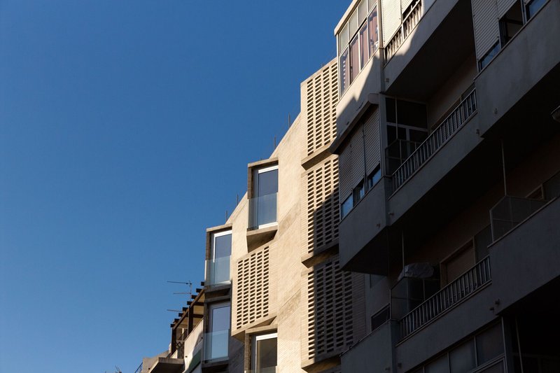 Close-up of the perforated brick screen elements alternating with recessed glazed openings in afternoon light
