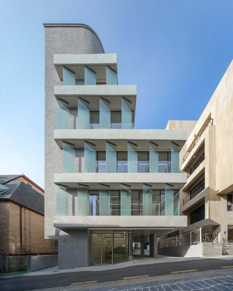 Street view of the grey brick facade with stacked balconies and angled window openings under a clear blue sky