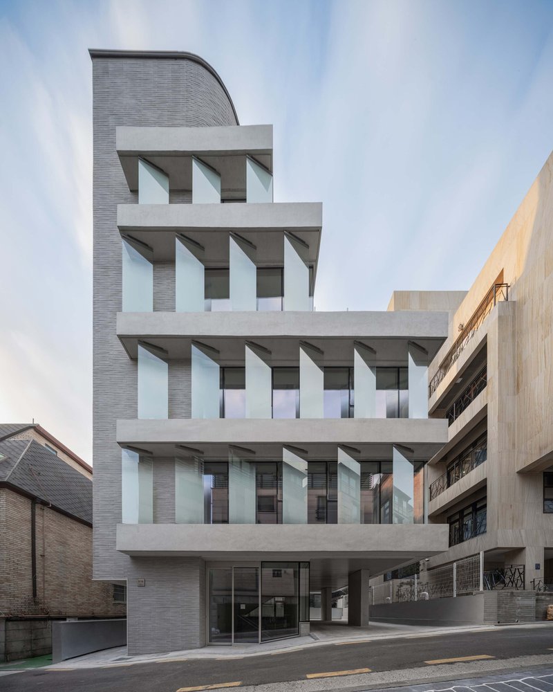 Frontal view of the facade showing four floors of concrete balconies with recessed glazing and grey brick cladding