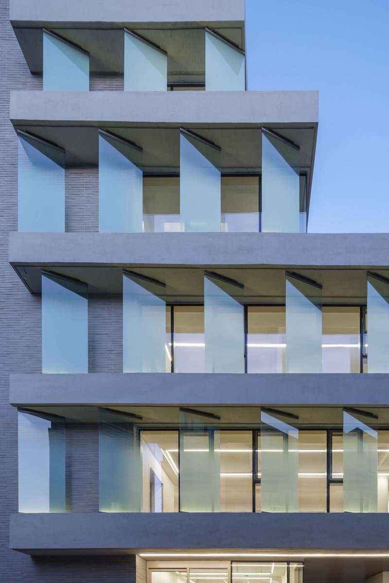 Close-up of the facade balconies with angled glass panels and interior lights visible at dusk