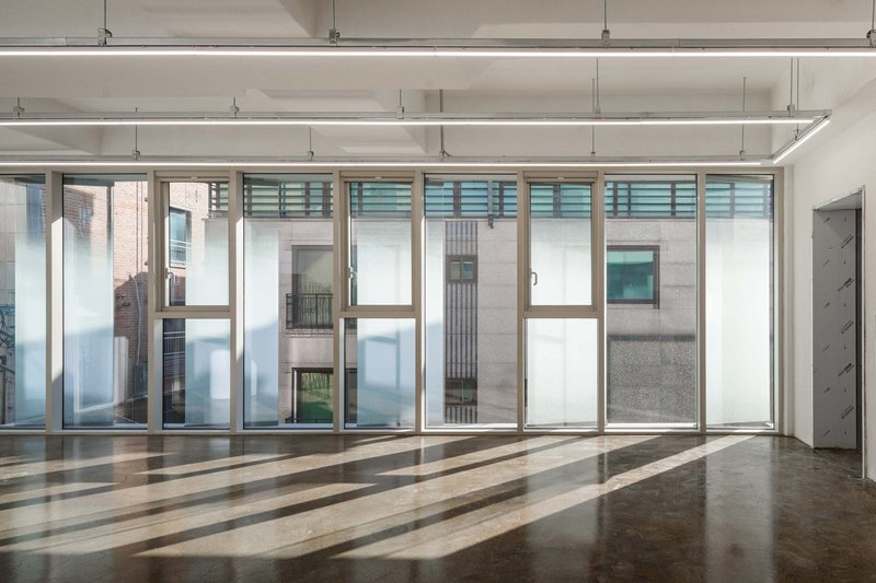 Interior space with full-height glazed walls, exposed ceiling beams, and striped sunlight patterns on polished concrete floor