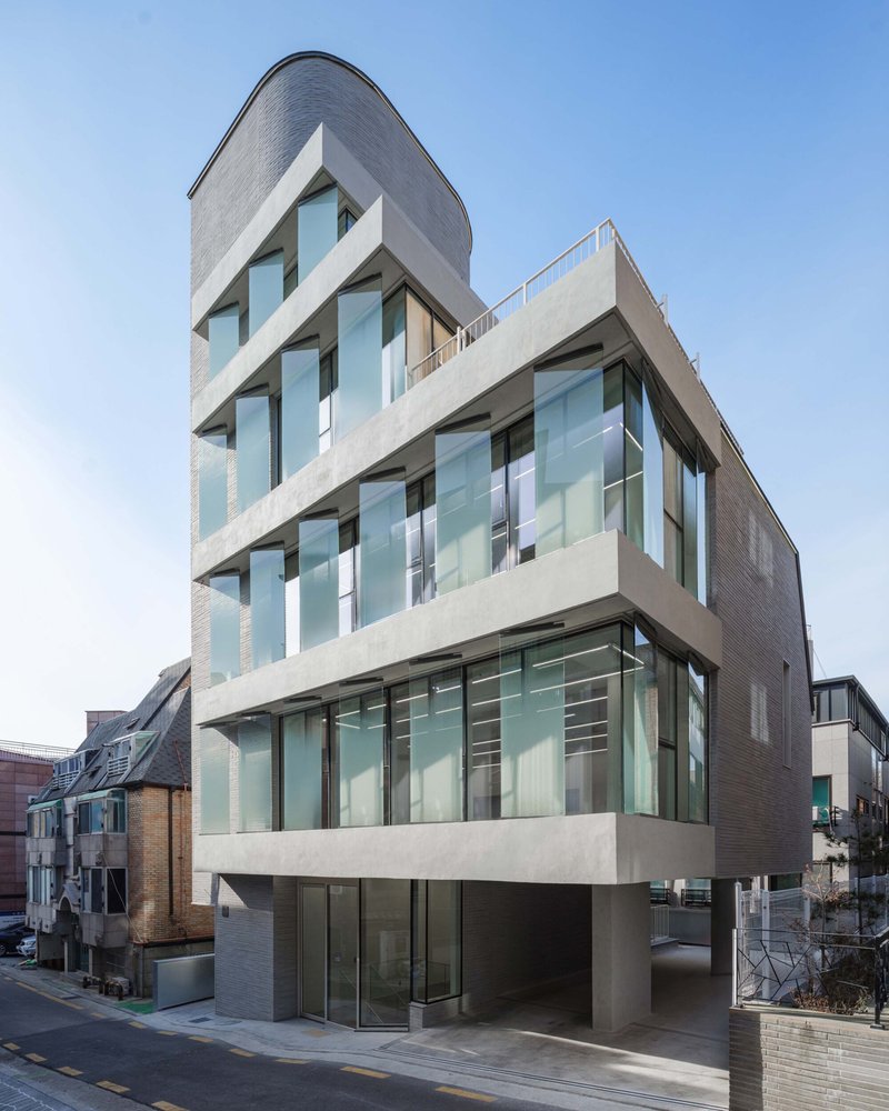 Street view of the concrete and glass facade with zigzagging balconies and a curved top floor under a clear sky