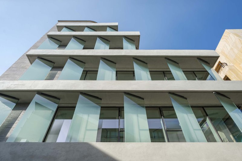 Upward view of the angled glass balconies projecting from white concrete slabs in bright daylight