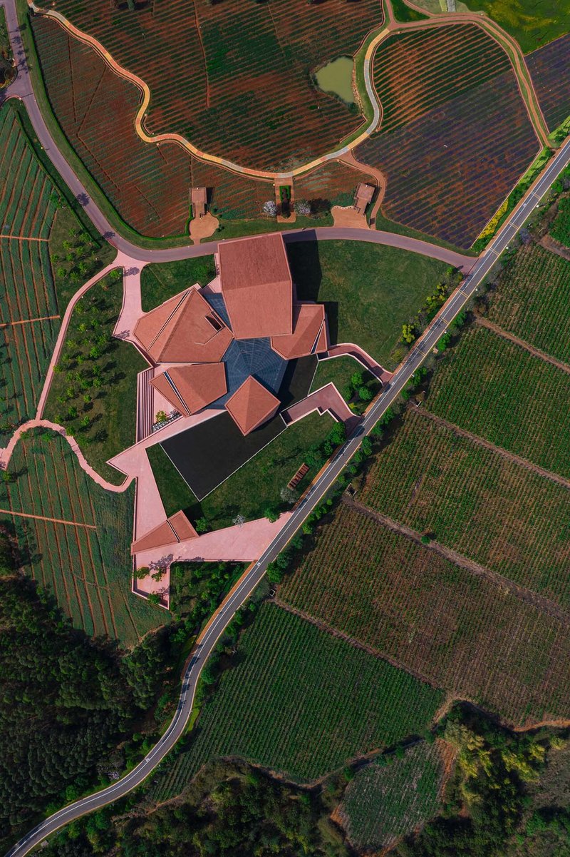 Drone view showing the angular red roofs and curving boundary walls amid farm plots