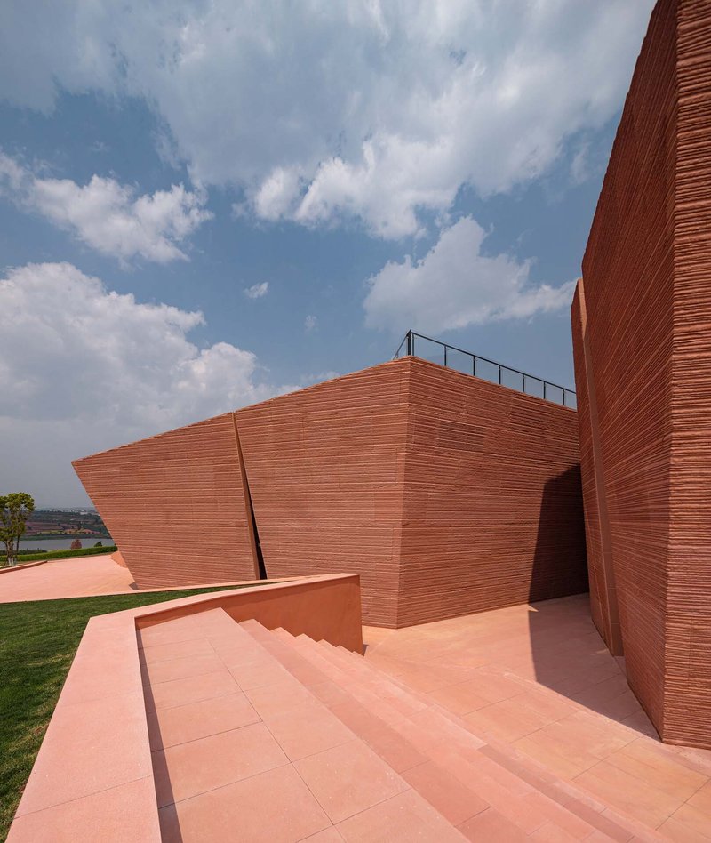 Rooftop terrace with salmon-colored paving and angled red brick walls under blue sky