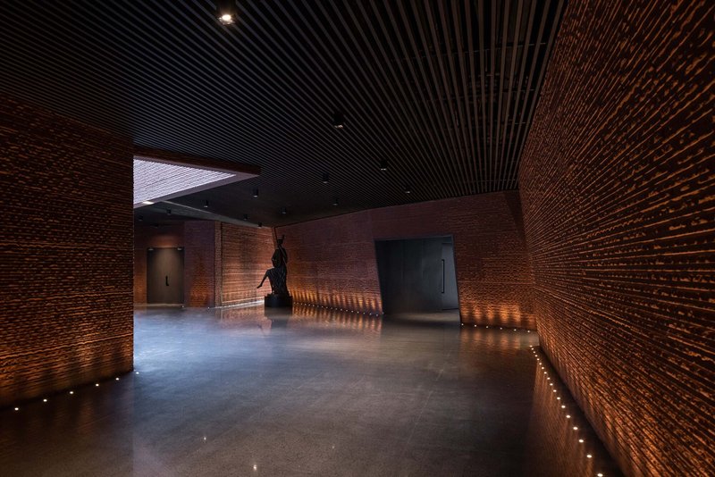 Interior gallery with textured brick walls, black slatted ceiling and recessed floor lighting