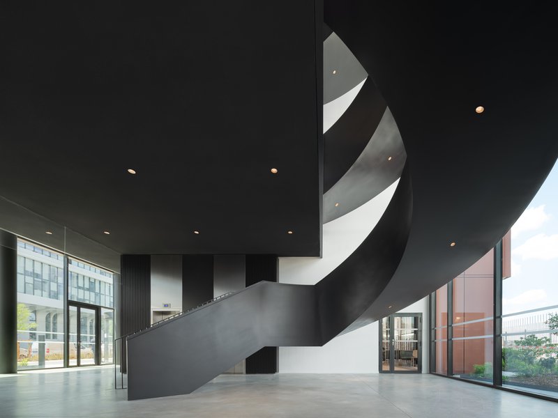 Interior lobby with black ribbon staircase spiraling beneath recessed ceiling downlights and glazed walls