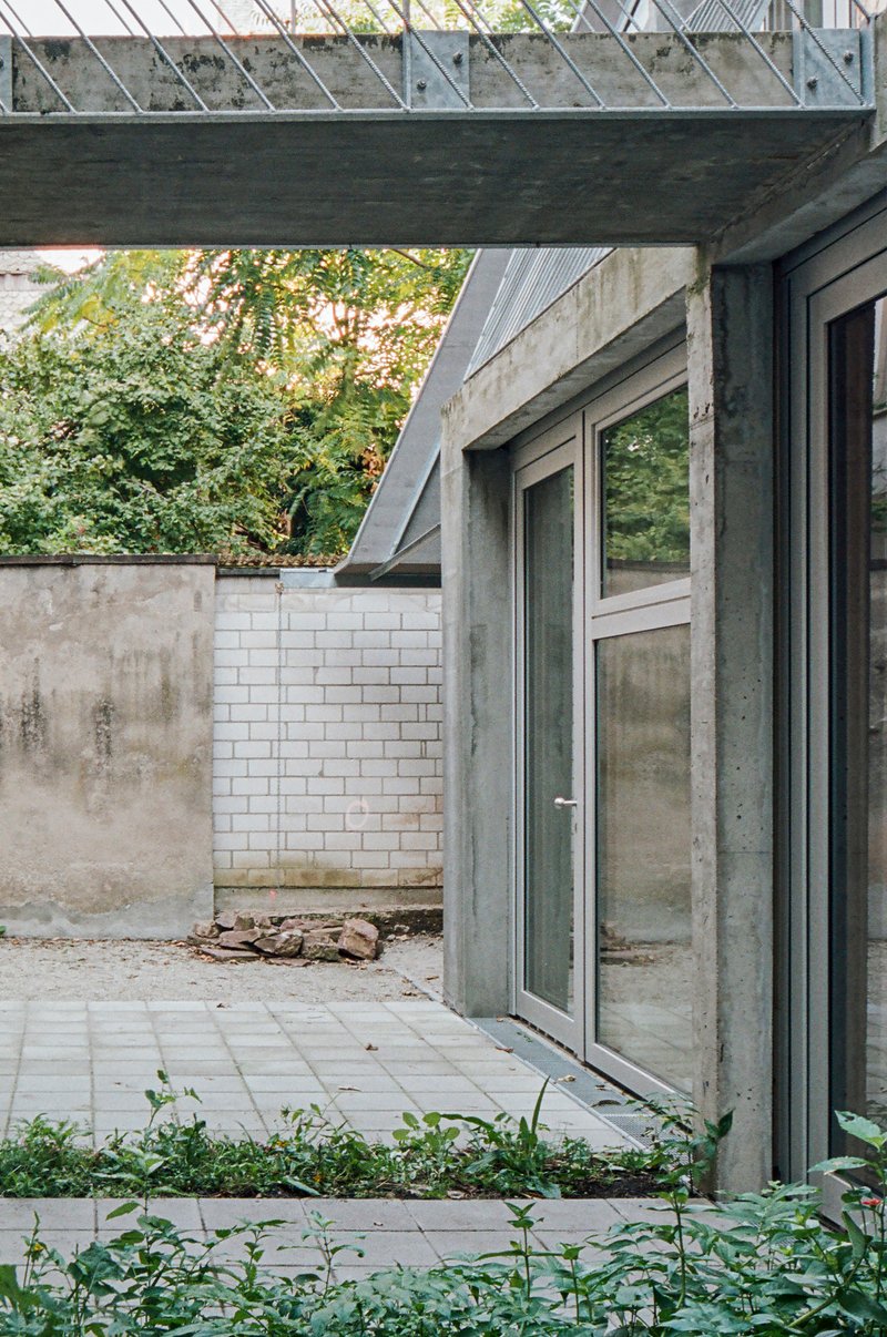 Courtyard terrace with concrete doorframe, white brick wall, and overhead metal grating in afternoon light
