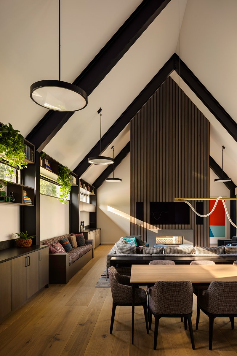 Open-plan living and dining space with black timber trusses and ribbed accent wall catching afternoon sun
