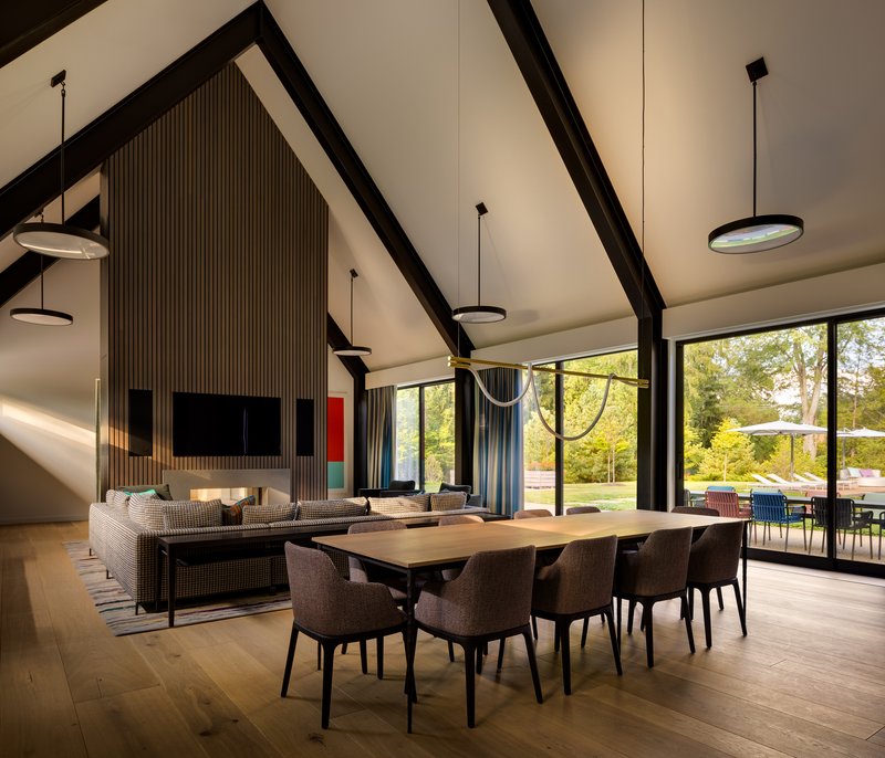 Open-plan dining and living space with exposed black timber trusses and garden views through glazed walls