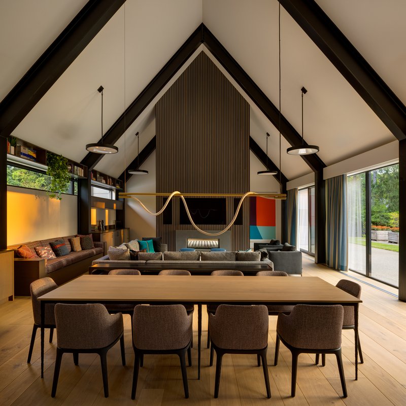 Dining table in front of vertical timber slat wall with embedded fireplace and television at dusk