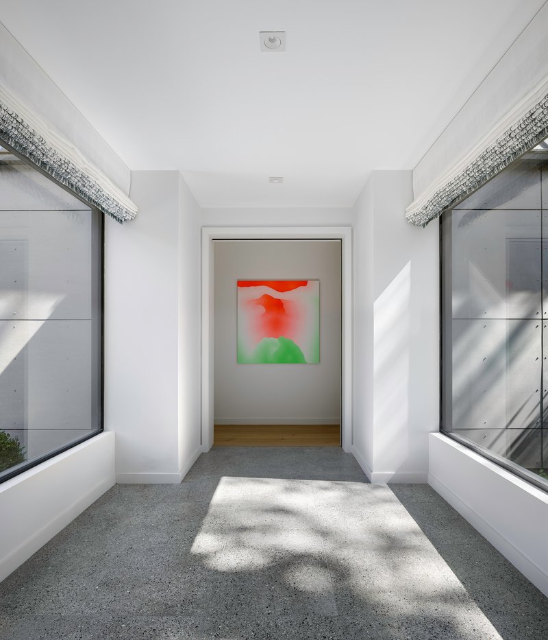 White corridor with flanking windows and dappled sunlight falling across the terrazzo floor