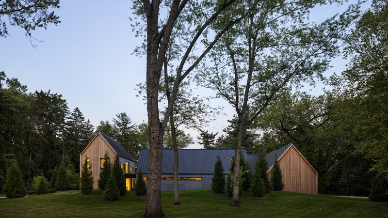Long facade with illuminated windows flanked by timber-clad gabled volumes under a cloudy sky