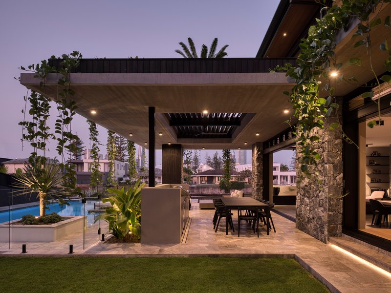 Covered outdoor dining terrace with stone columns wrapped in vines at dusk