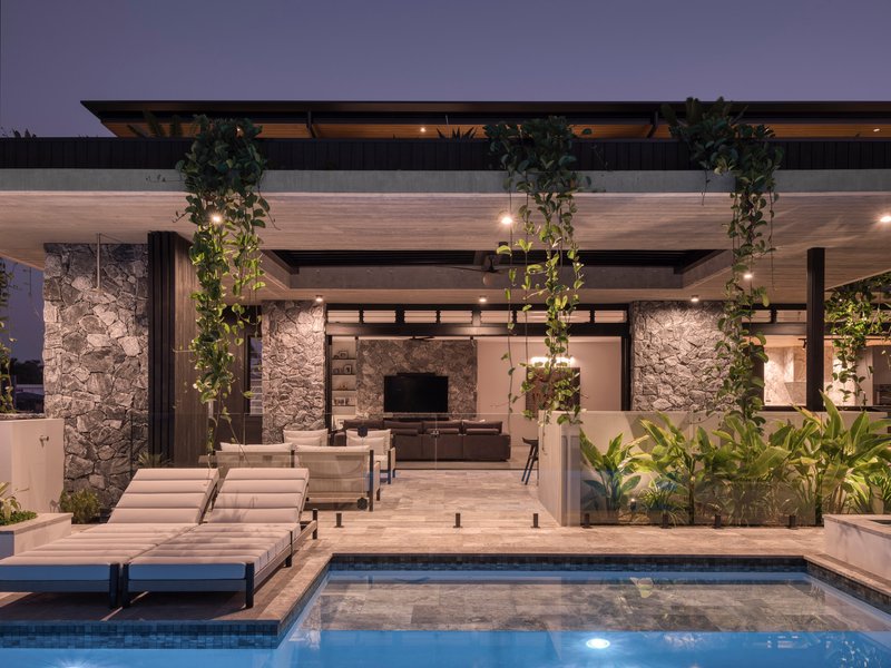 Pool deck with stone columns, hanging plants and views into living room at twilight