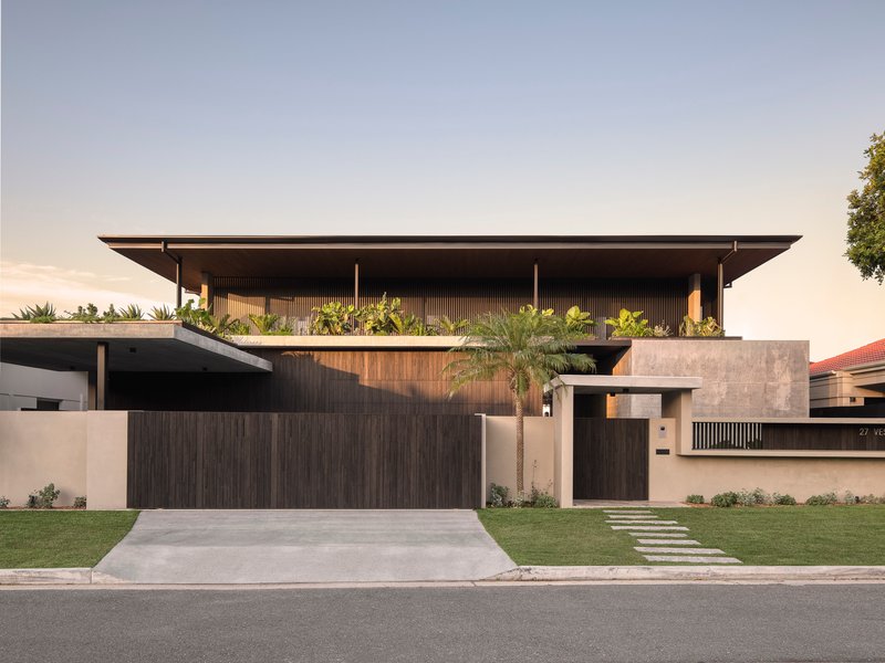Street view of the two-level facade with timber cladding, concrete walls and planted upper terrace at dusk