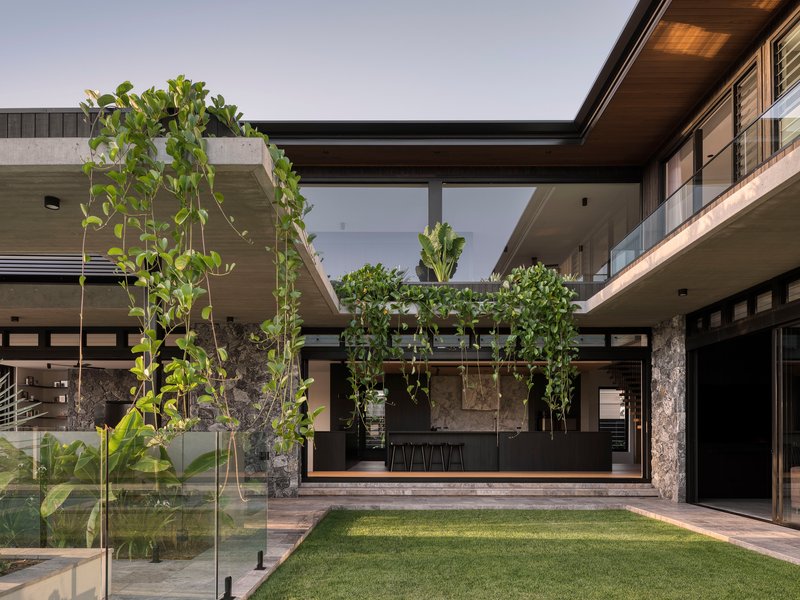 Central courtyard with lawn, young trees and glazed kitchen opening beneath exposed timber ceiling