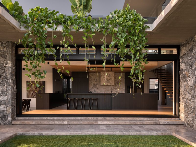 View into the open kitchen with hanging vines, stone columns and dark cabinetry from the courtyard