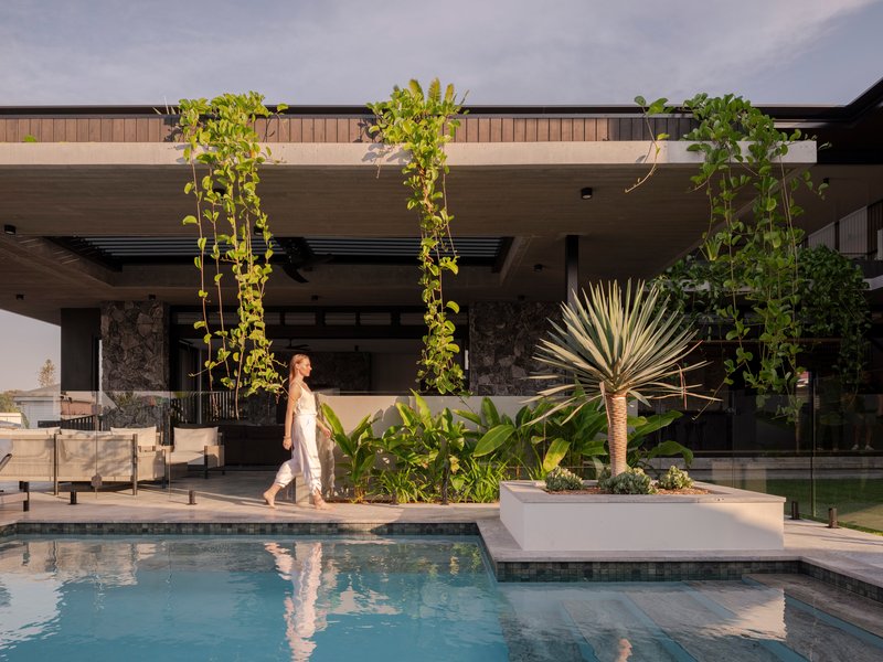 Pool deck with planted bed and person walking past hanging vines and stone-clad columns