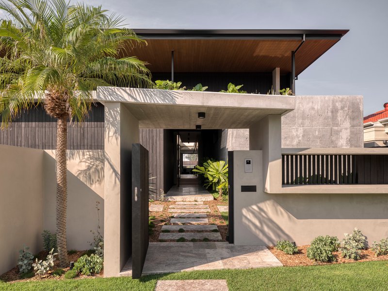 Entry portal with concrete canopy, stepping stones and palm tree casting afternoon shadows