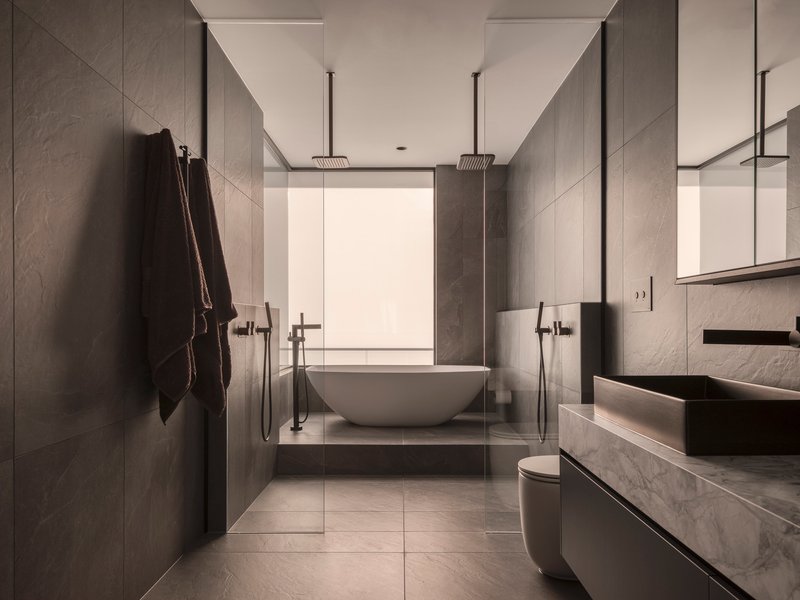 Bathroom with grey stone panels, freestanding tub, glass shower enclosure and dual rainfall showerheads