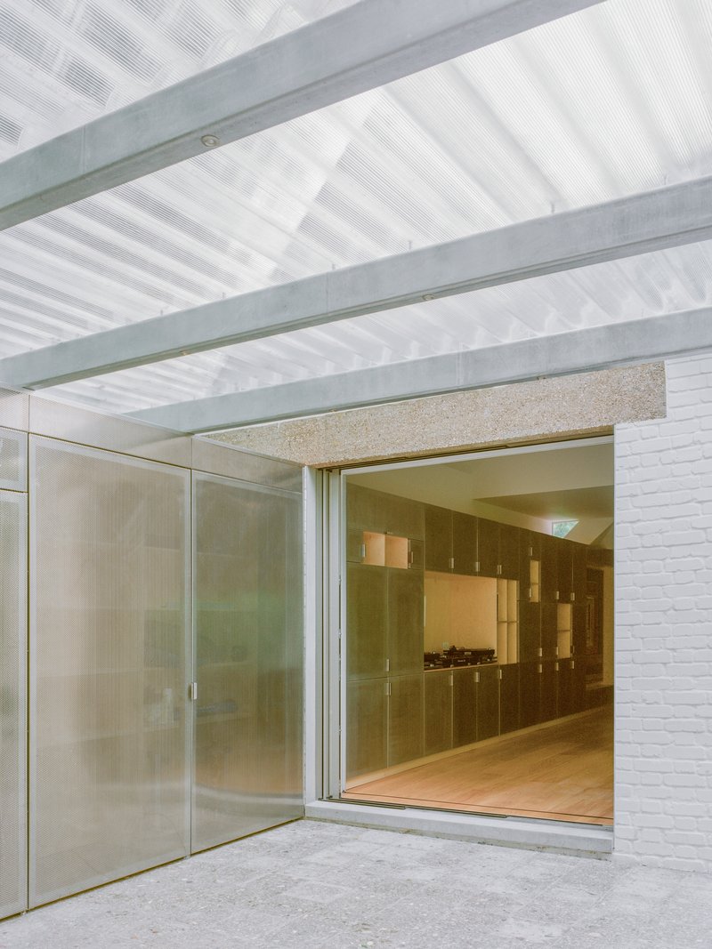 Covered threshold with exposed steel beams and corrugated polycarbonate ceiling opening to interior timber cabinetry