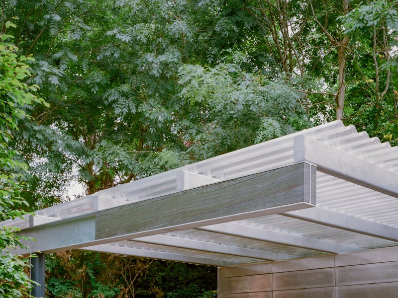 Canopy structure with exposed timber beams and translucent ribbed panels framed by surrounding trees