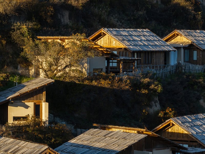 Gabled timber structures with weathered metal roofs scattered across terraced slopes in golden afternoon light